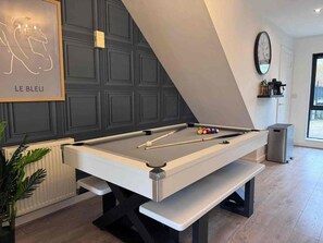 Ett biljardbord med modern design, ett inramat konstverk på väggen och en klocka.