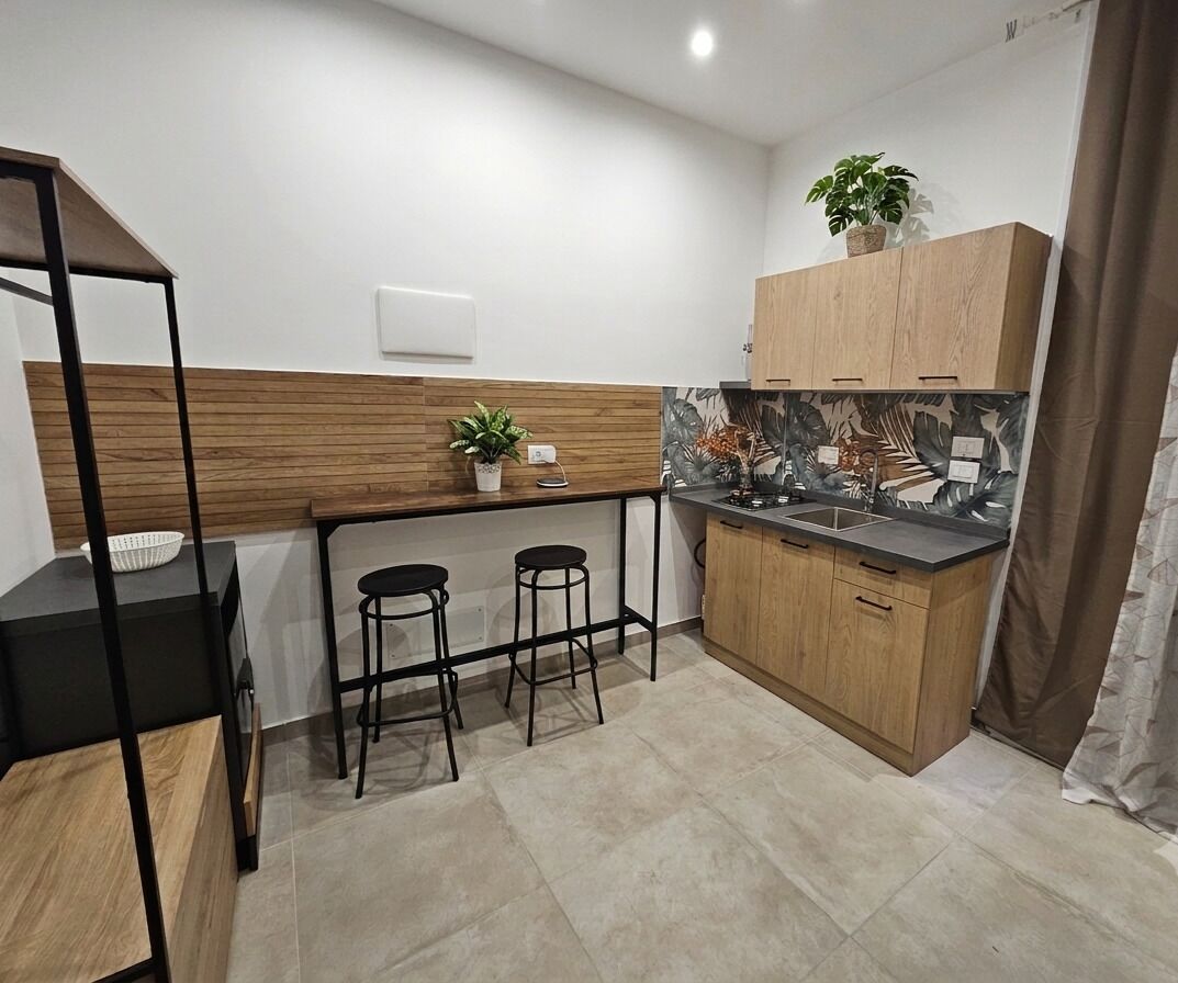 A compact kitchen with a wooden countertop, two stools, and a potted plant.