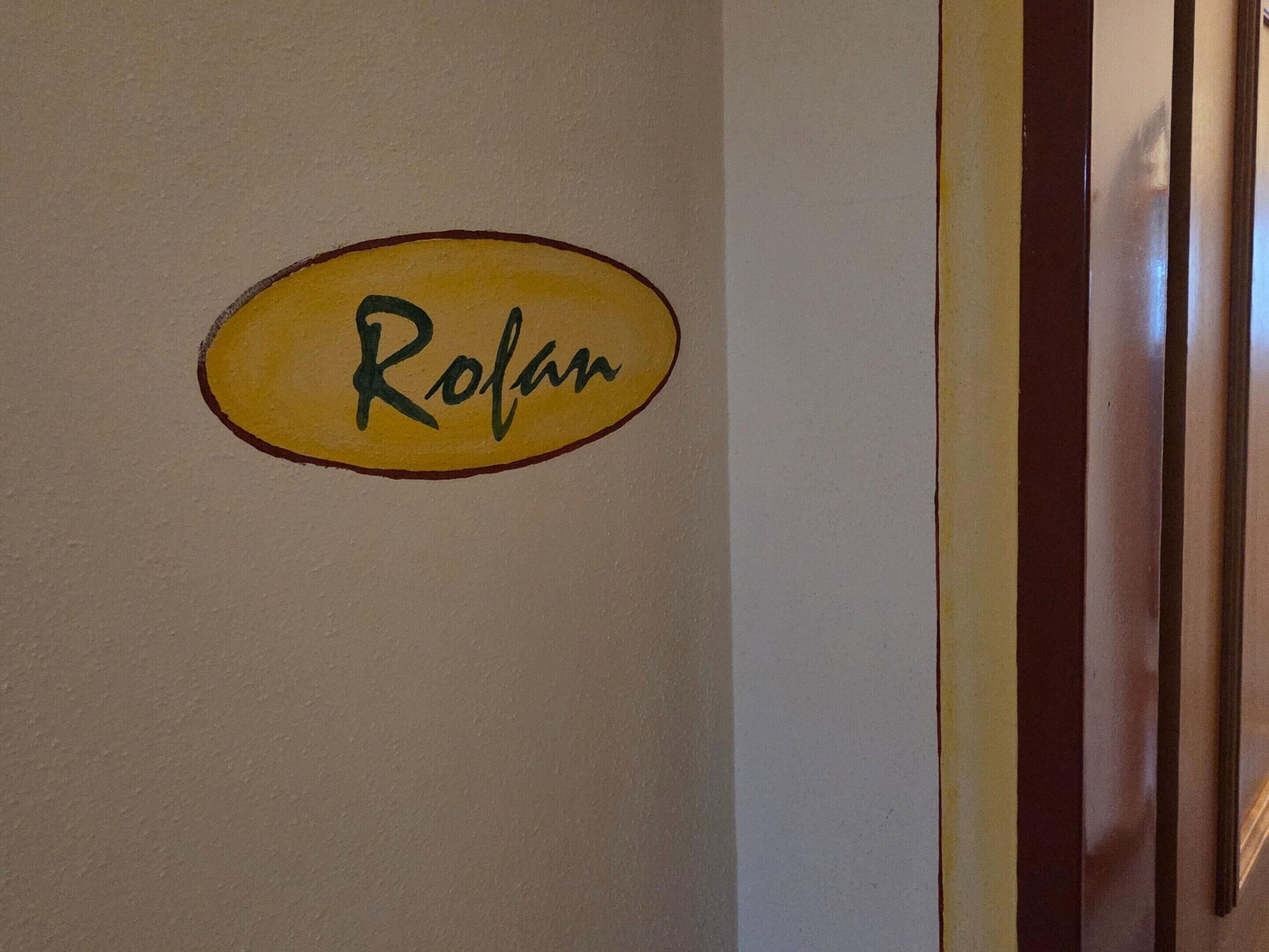 A wall with a nameplate that reads 'Rolan' in a yellow oval.