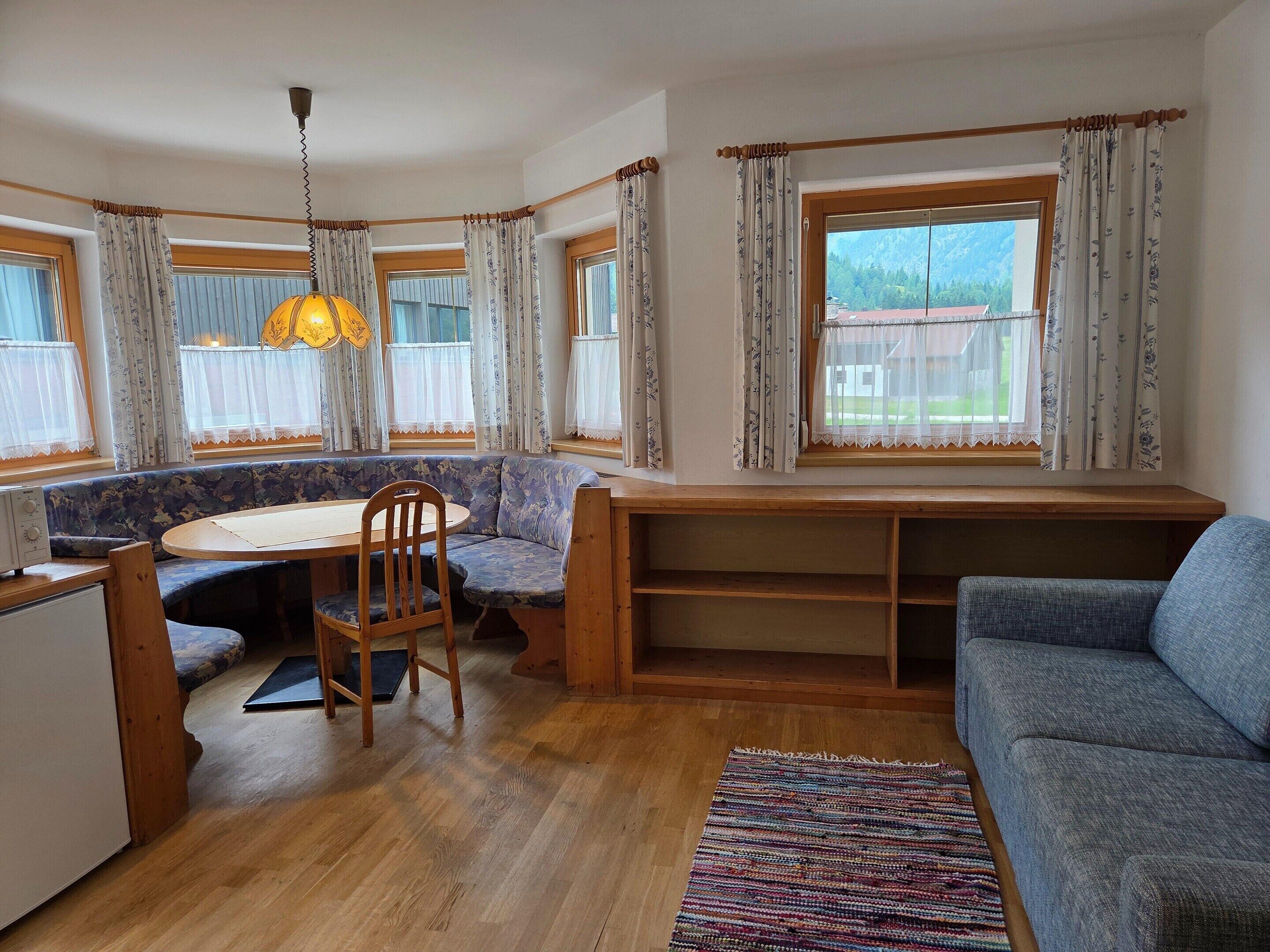 A cozy room with a wooden dining table, a blue sofa, and a window with curtains.