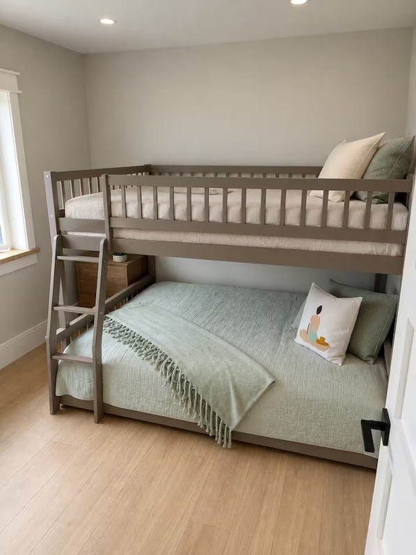 A bunk bed with a ladder, a bedside table, and a window with curtains.