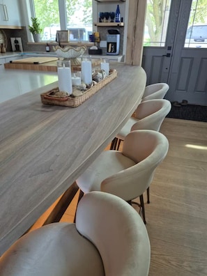 A long dining table with a woven tray and candles, surrounded by cushioned chairs.