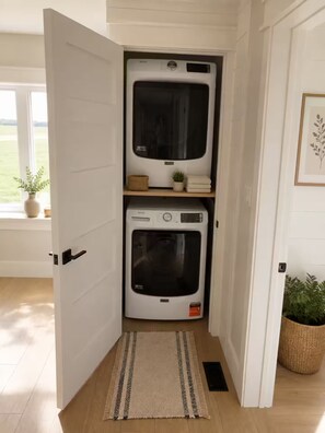 A laundry room with two stacked washers and dryers, a small plant on the top shelf, and a door leading to a hallway.