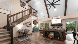 A spacious living area with a wooden staircase, a fireplace, and a large window overlooking a deck. - The Lazy Beaver Lodge Hot Tub (Hollister)