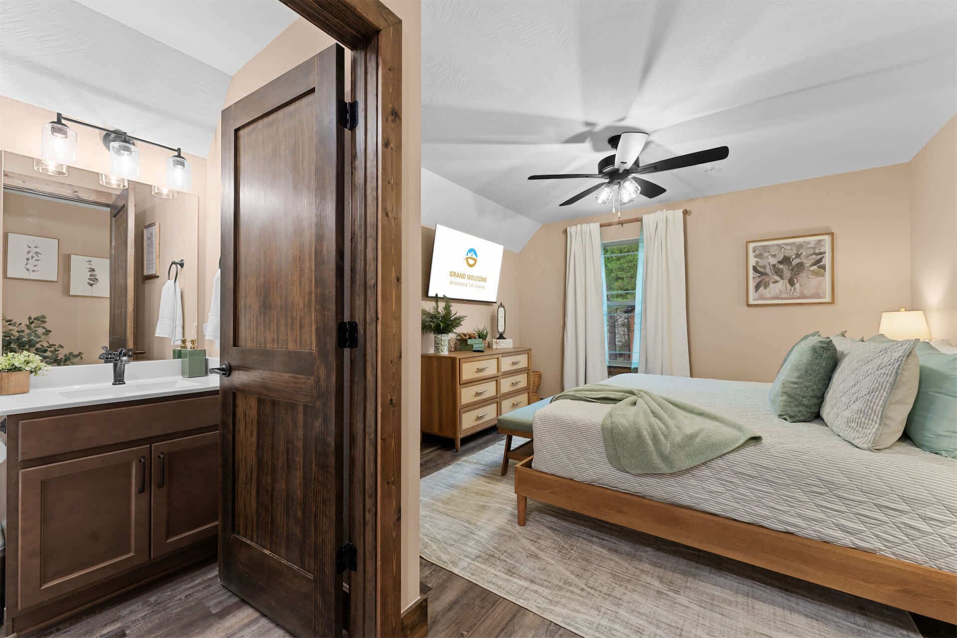 Un dormitorio con cama, ventilador de techo, cómoda, tocador con espejo y televisor.