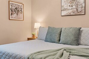 A bedroom with a bed, pillows, a bedside table with a lamp, and two framed artworks on the wall. - The Lazy Beaver Lodge Hot Tub (Hollister)