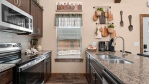 A kitchen with a built-in oven, a stovetop, a sink, and a window with blinds. - The Lazy Beaver Lodge Hot Tub (Hollister)