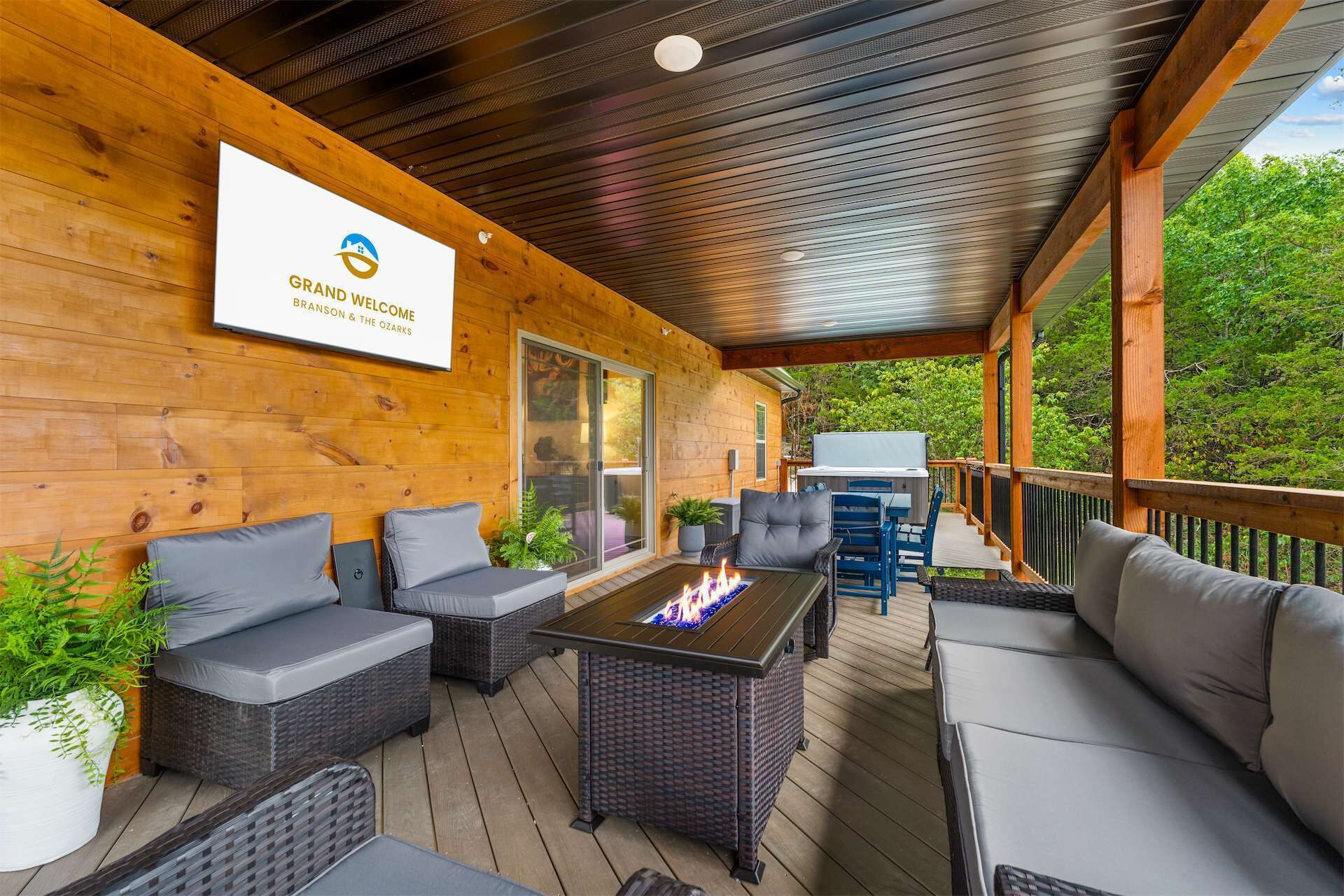 A covered outdoor seating area with wicker furniture, a fire feature, and a sign for Grand Welcome Branson & The Ozarks.