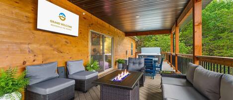 A covered outdoor seating area with wicker furniture, a fire feature, and a sign for Grand Welcome Branson & The Ozarks.