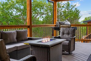 An outdoor deck with a grill, a cushioned seating area, and a fire feature. - The Lazy Beaver Lodge Hot Tub (Hollister)