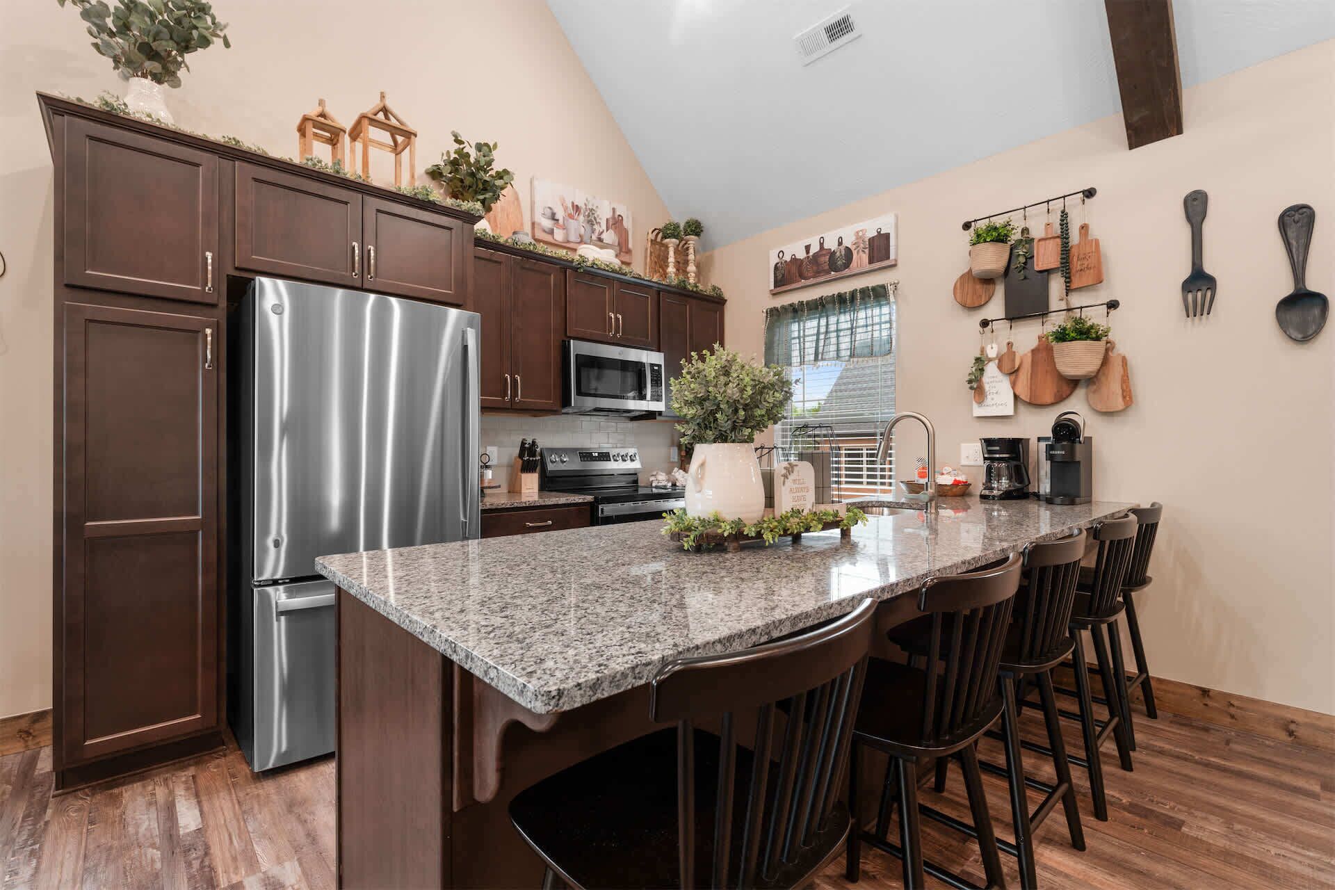 A kitchen with a granite countertop, stainless steel refrigerator, wooden cabinets, and a bar area with stools.
