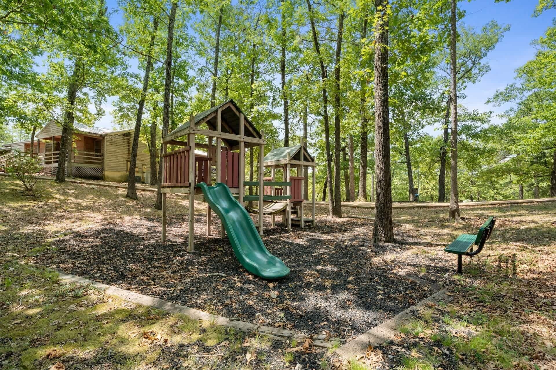 Un parque infantil con un tobogán y un banco, rodeado de árboles.