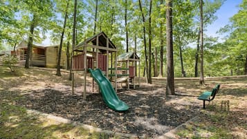 Un parque infantil con un tobogán y un banco, rodeado de árboles.