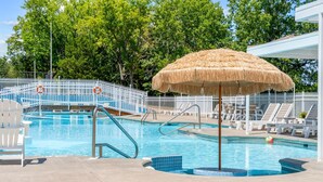 Ein Swimmingpool mit einem Reetdachschirm, Liegestühlen und einem weißen Zaun.
