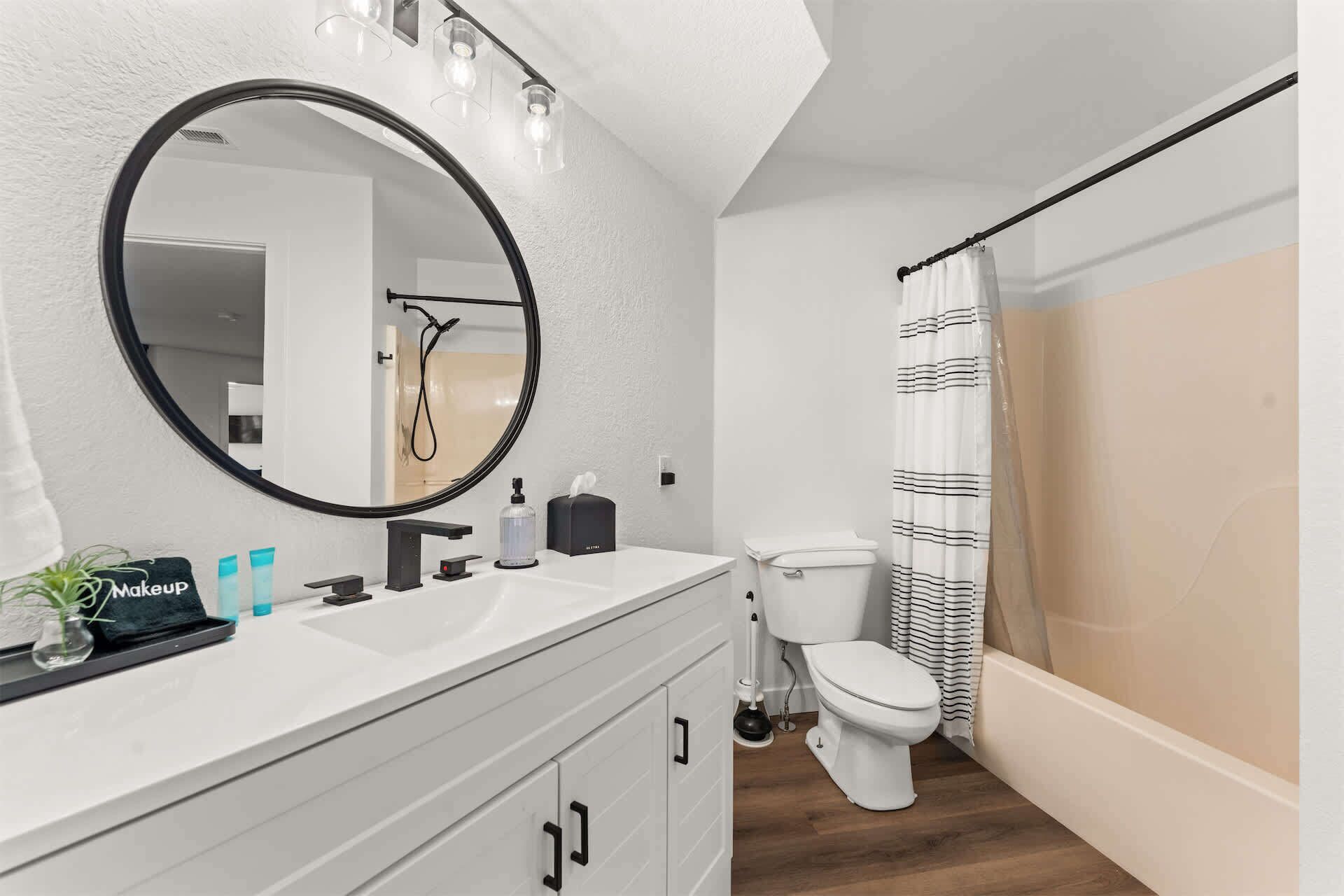 A modern bathroom with a round mirror, a white sink, a toilet, and a shower curtain.