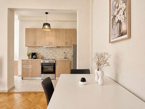 A modern kitchen with wooden cabinets, a built-in oven, and a dining area with a white table and chairs. - Athens Base Αpt - Near Metro & Museum by ΜΡS (Athina)