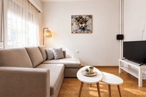 A modern living room with a sofa, a coffee table, a flat-screen TV, and a painting on the wall. - Athens Base Αpt - Near Metro & Museum by ΜΡS (Athina)