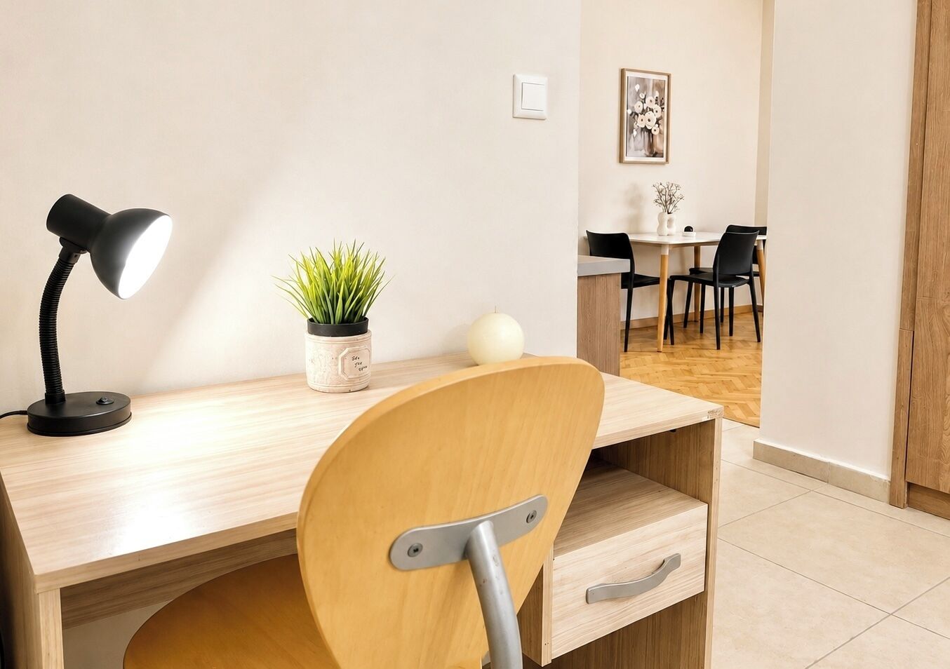 Un espacio de oficina moderno con un escritorio, una silla, una lámpara, una planta en maceta y una zona de comedor al fondo.