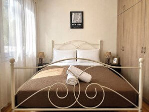 A neatly made bed with a brown bedspread and white pillows, a framed map of New York on the wall, and a wooden wardrobe with metal handles. - Athens Base Αpt - Near Metro & Museum by ΜΡS (Athina)