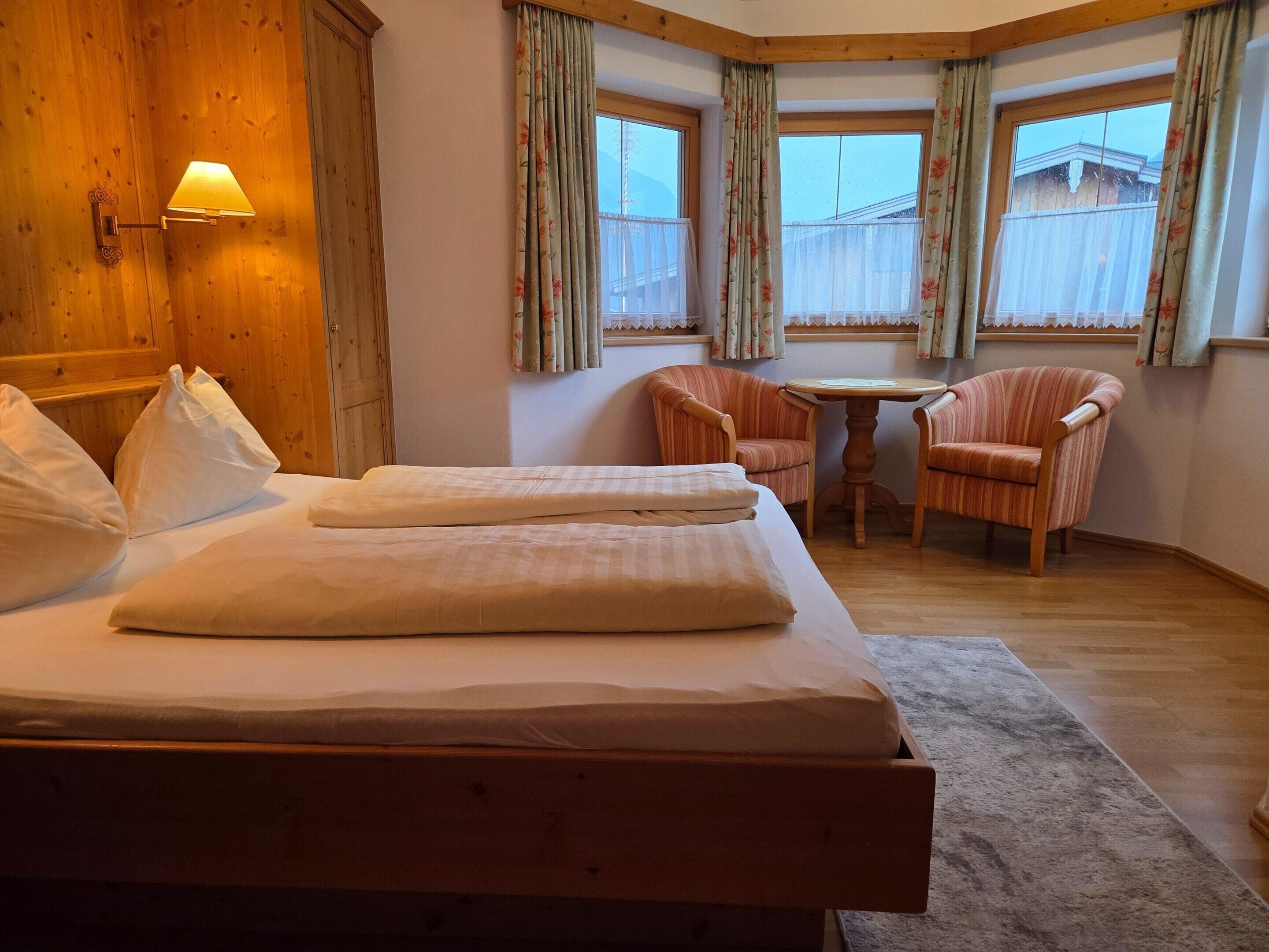 A hotel room with a bed, two chairs, a small table, and a window with curtains.