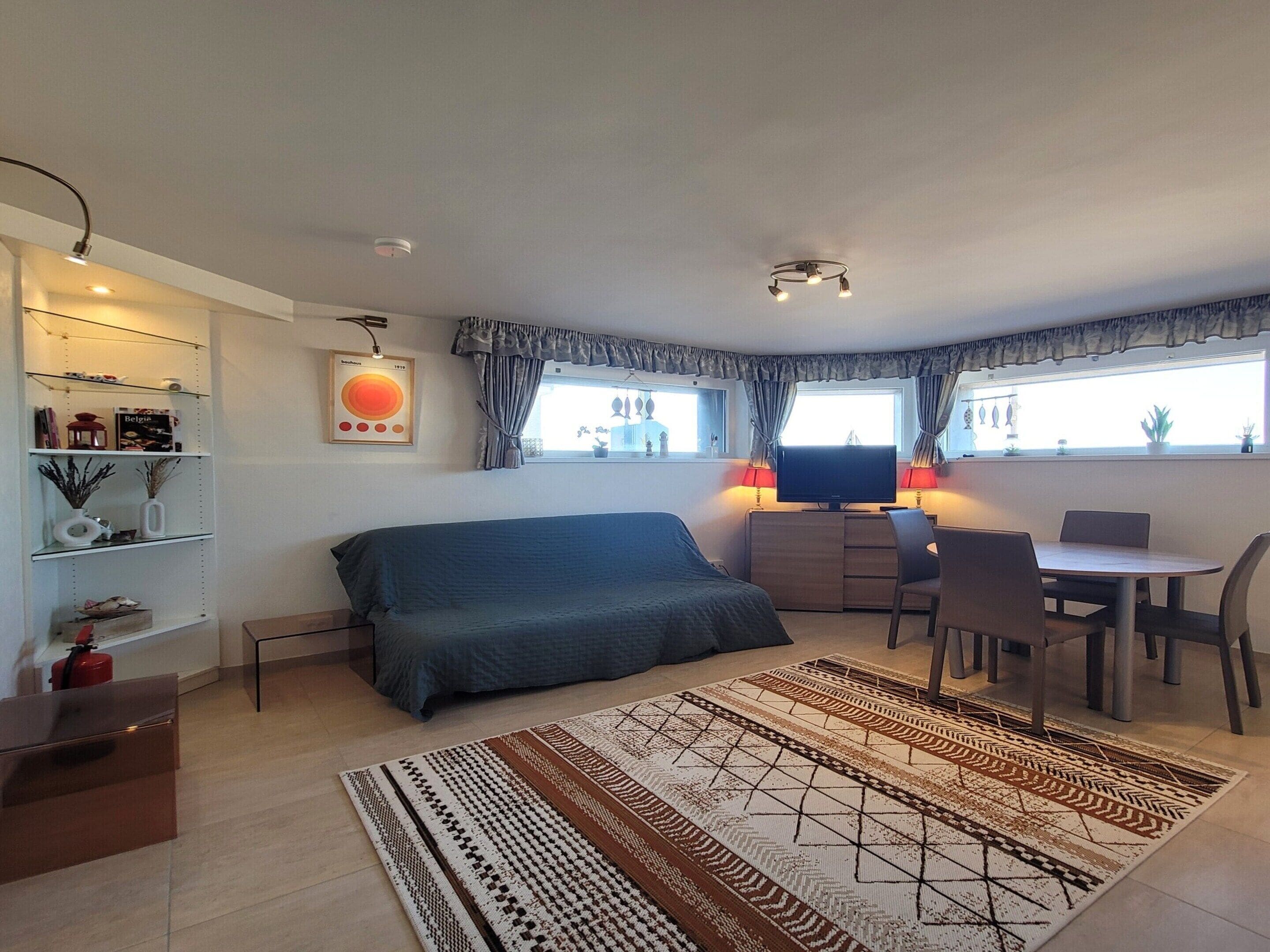 Ein kleines Schlafzimmer mit Bett, Nachttisch, Fernseher und einer Essecke mit Stühlen und Tisch.