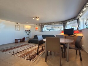A modern living room with a sofa, a dining table with chairs, a television, and a patterned rug. - Coastal Comfort Middelkerke (Middelkerke)