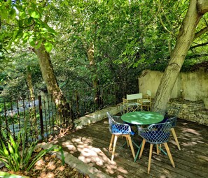 An outdoor patio with a table and chairs, surrounded by trees and a stone wall. - Mas La Fontaine de Pernes, right on the banks of the Sorgue River, with a pool, sleeps 12, 6 bedrooms, 5 bathrooms (Pernes-les-Fontaines)