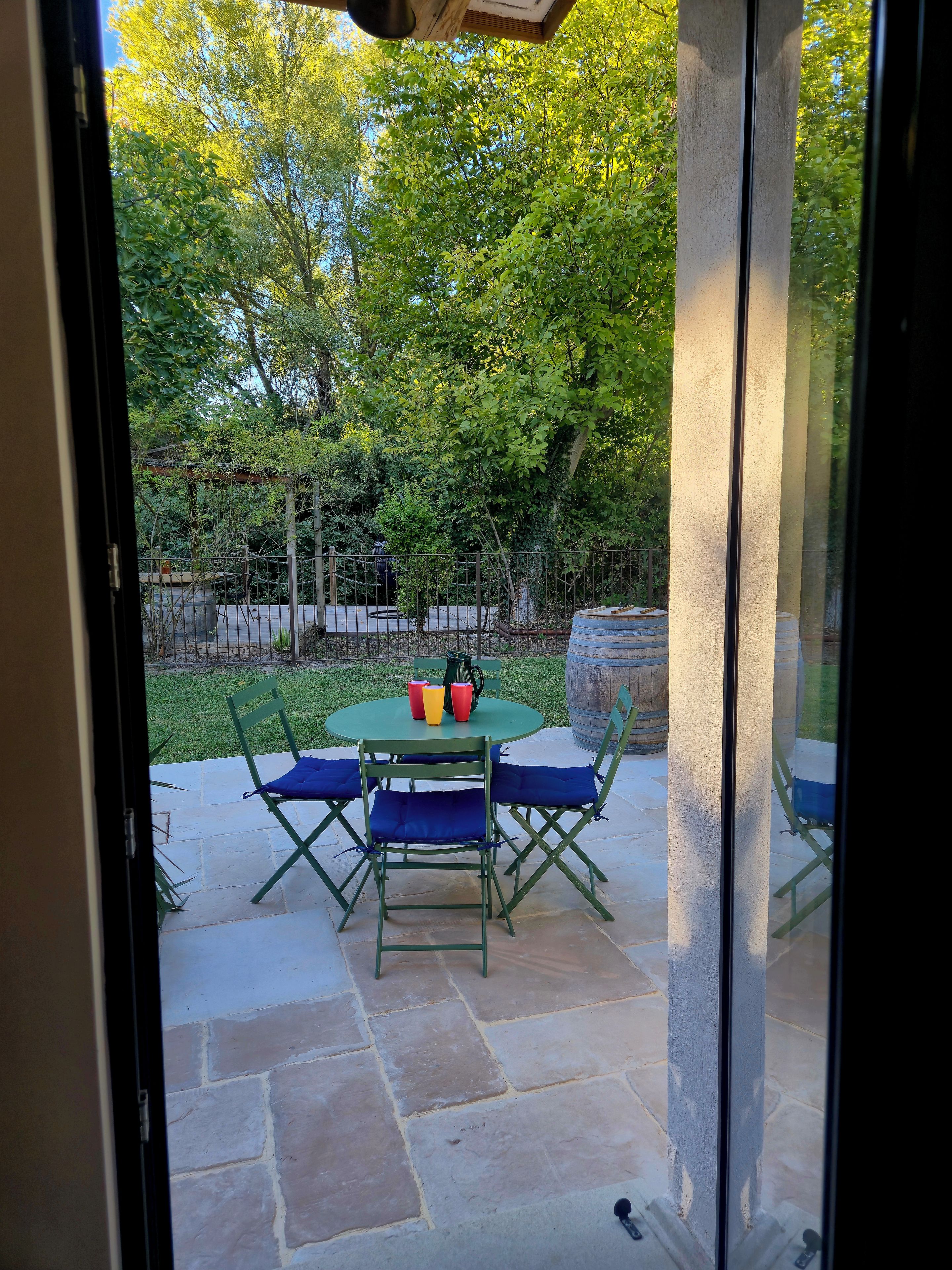Eine Terrassenfläche mit Tisch und Stühlen, einer Feuerstelle und Blick auf einen Garten durch eine Glastür.
