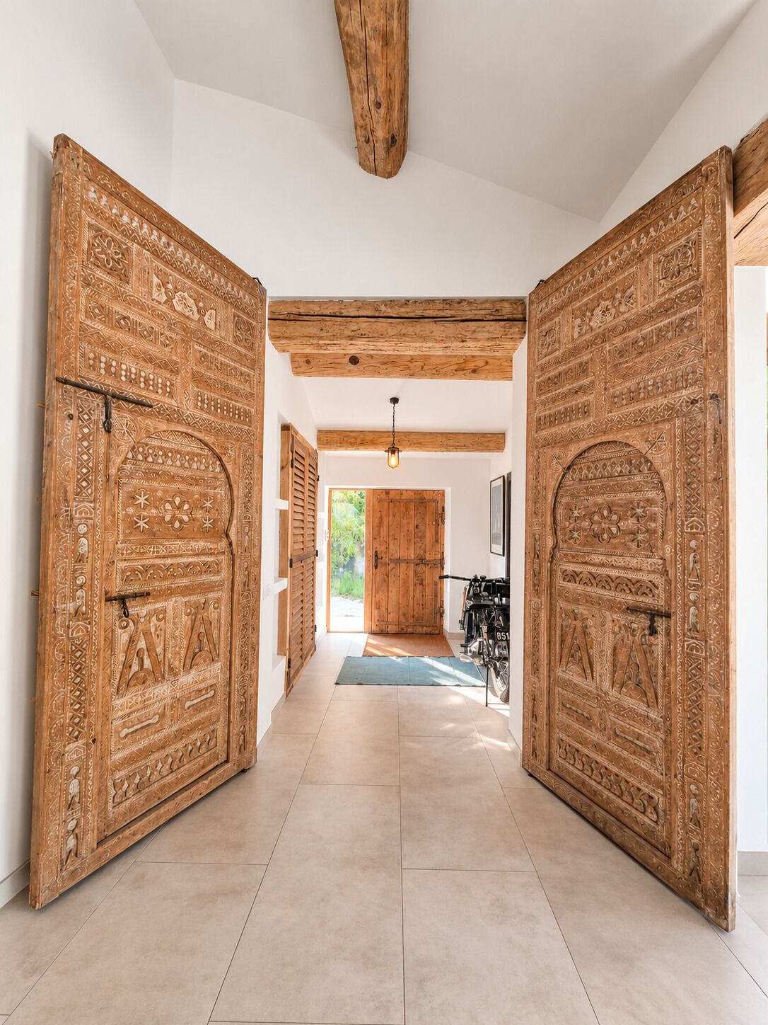 Un pasillo con puertas de madera grandes y talladas, que conduce a una habitación con una bicicleta y una puerta.