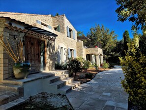 A stone building with a courtyard, steps leading to the entrance, and a potted plant.