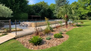 A landscaped garden with a pool, surrounded by a metal fence, and various plants and trees.