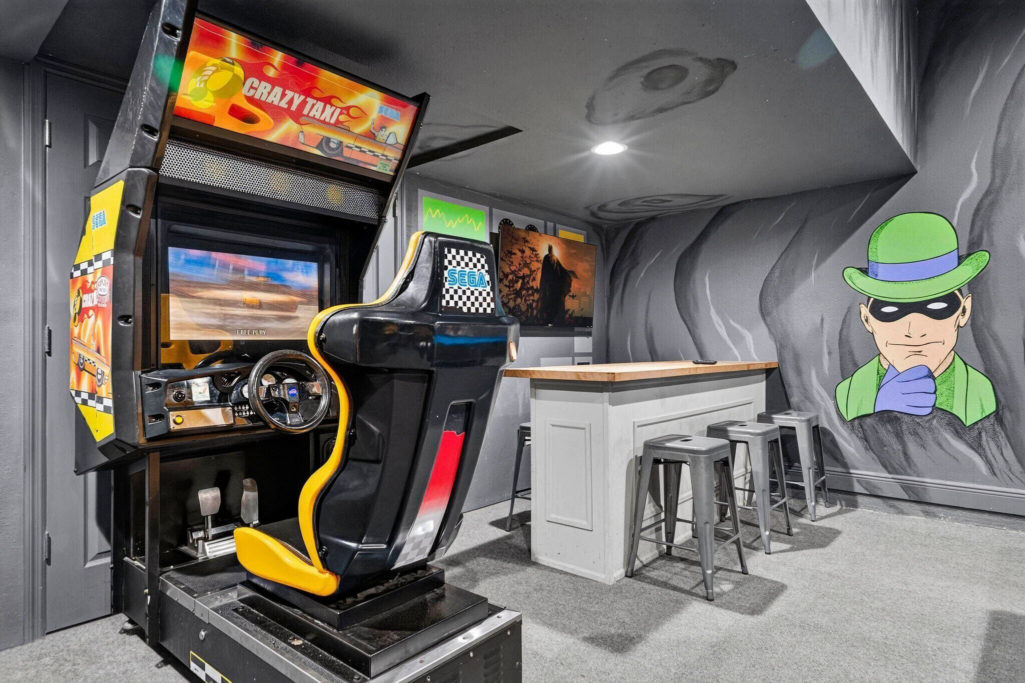 A gaming arcade with racing and action games, a bar area, and a cartoon character mural.