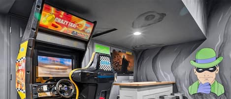 A gaming arcade with racing and action games, a bar area, and a cartoon character mural.