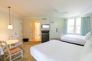 Ein Hotelzimmer mit Bett, Schreibtisch, Stuhl, Fernseher und Deckenventilator.