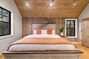 A bedroom with a wooden ceiling, a large bed with white and orange bedding, and a nightstand with a plant. - New Rustic Luxury Cabin | Minutes to Blue Ridge (Blue Ridge)