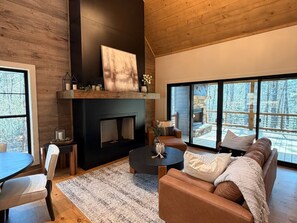 A modern living room with a fireplace, seating area, and large windows offering a view of the outdoors. - New Rustic Luxury Cabin | Minutes to Blue Ridge (Blue Ridge)