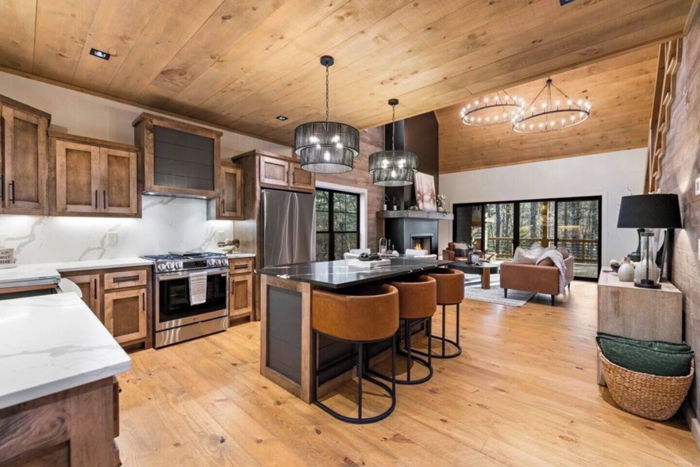 A spacious kitchen with wooden cabinets, a central island with stools, stainless steel appliances, and pendant lighting.