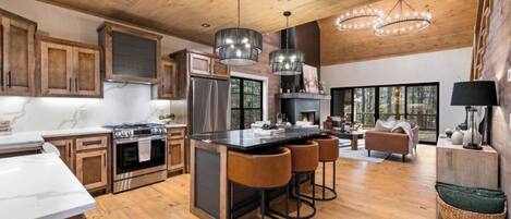A spacious kitchen with wooden cabinets, a central island with stools, stainless steel appliances, and pendant lighting.