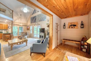 A spacious living area with a high ceiling, wooden beams, a dining table, a sofa, and a television. - Bear Ridge-Private Cabin-Mountain Views-Hot Tub! (Blairsville)