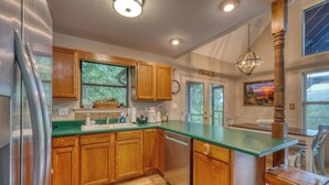 A kitchen with wooden cabinets, a green countertop, a stainless steel refrigerator, and a hanging light fixture. - Bear Ridge-Private Cabin-Mountain Views-Hot Tub! (Blairsville)
