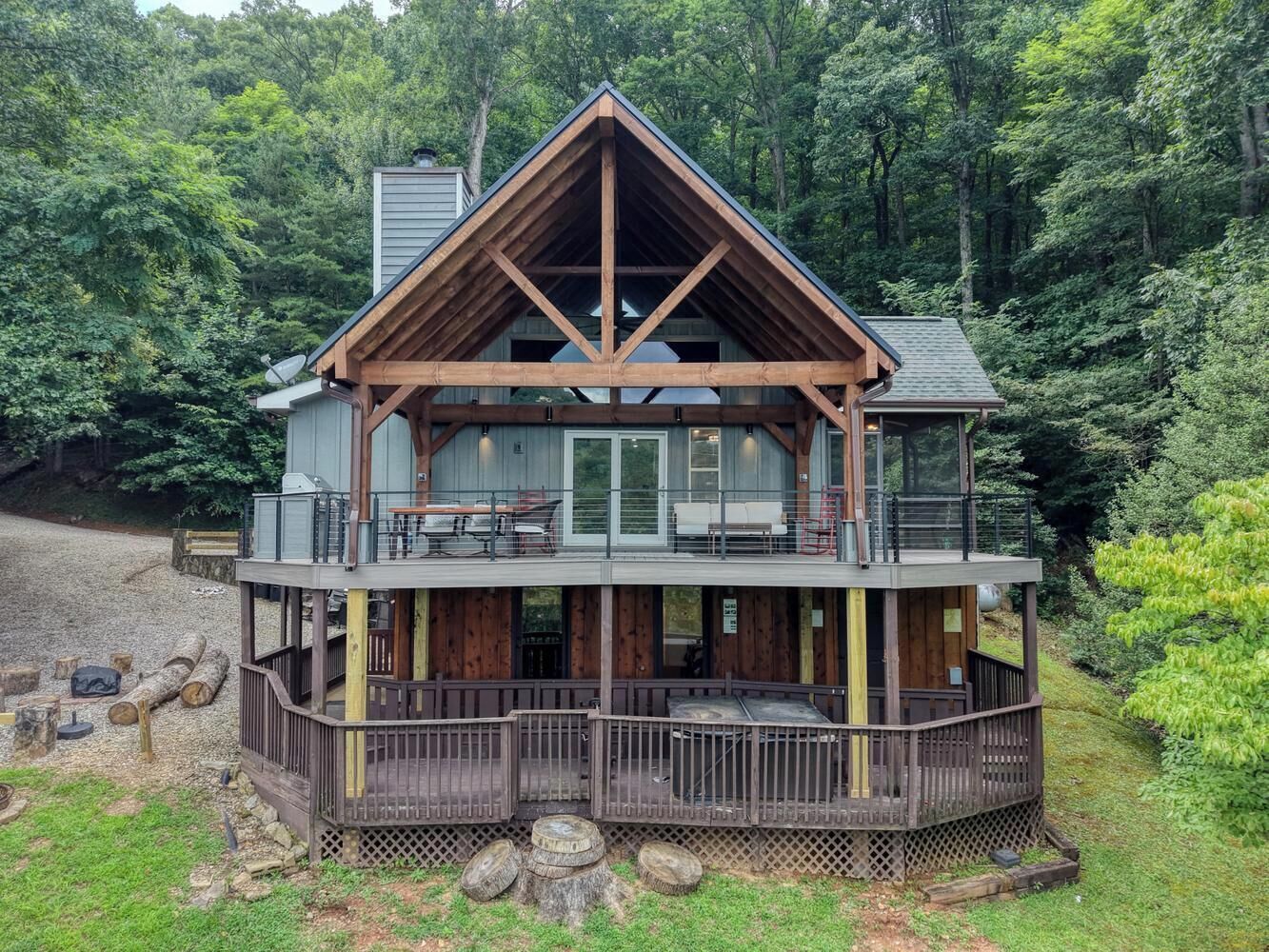 A two-story wooden cabin with a balcony and deck, surrounded by forest.