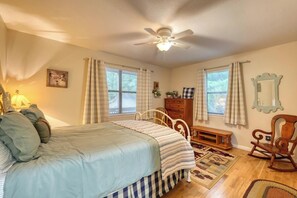 Ein Schlafzimmer mit einem Bett, einem Schminktisch, einem Stuhl, einem Deckenventilator und einem Fenster mit Vorhängen.