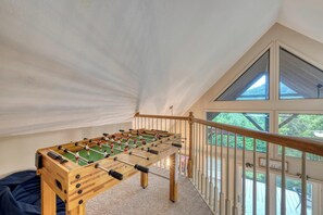 Une table de baby-foot dans une pièce dont le plafond est incliné et qui offre une vue sur la verdure à l’extérieur.