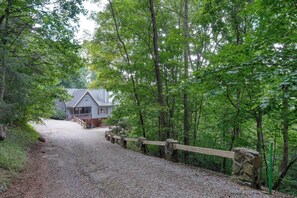 Ein Kiesweg führt zu einer rustikalen Holzhütte, umgeben von dichtem Wald.