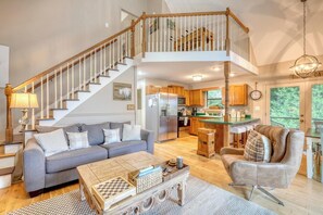 A spacious living area with a staircase leading to a loft, a kitchen with wooden cabinets, and a dining area with a view. - Bear Ridge-Private Cabin-Mountain Views-Hot Tub! (Blairsville)