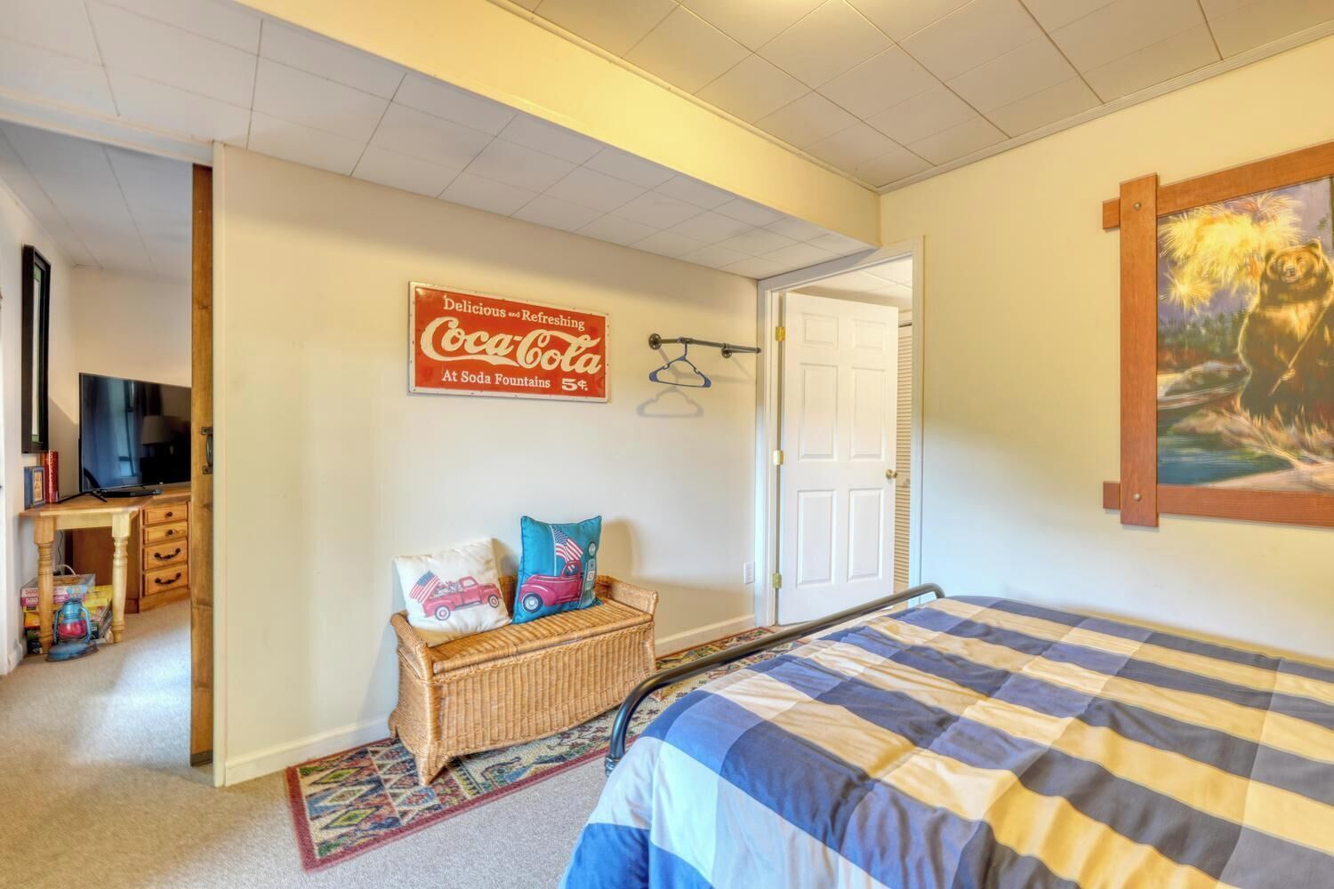 A bedroom with a bed, a television, a Coca-Cola sign, and a painting of a bear.