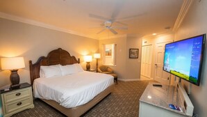 Una habitación de hotel con cama, lámparas de noche, escritorio con computadora, televisor y ventilador de techo.
