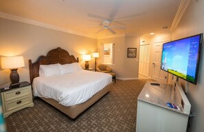 Una habitación de hotel con cama, lámparas de noche, escritorio con computadora, televisor y ventilador de techo.