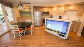 Una cocina moderna con armarios de madera, un refrigerador de acero inoxidable, un microondas y un televisor de pantalla plana.