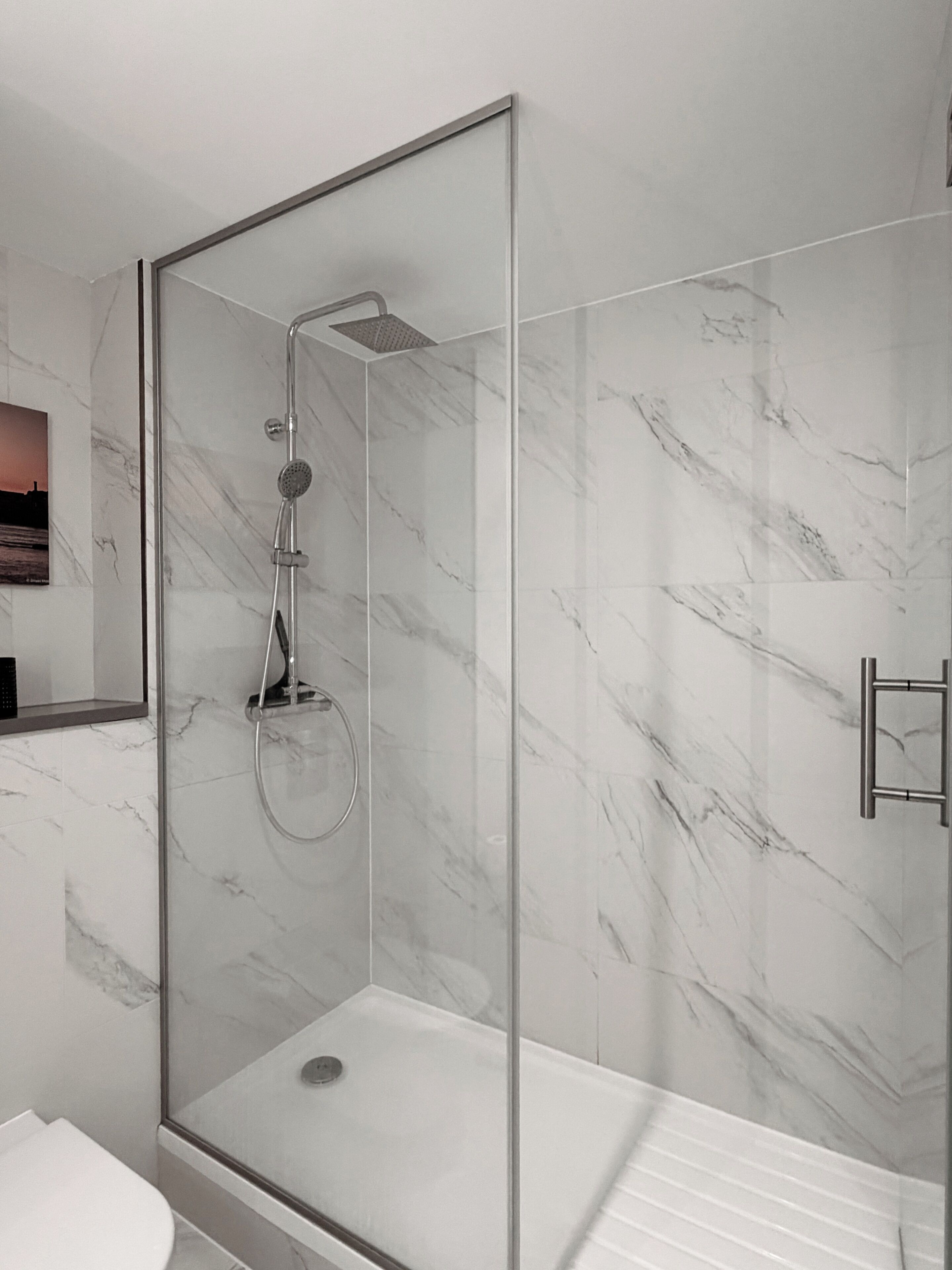 A modern bathroom with a glass-enclosed shower, marble walls, and a white sink.